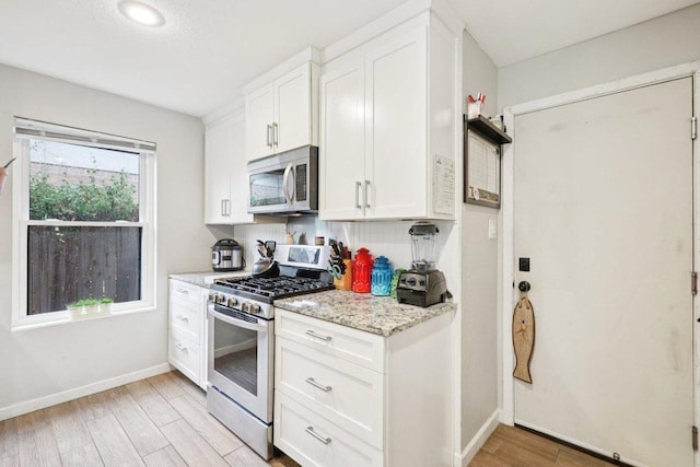 6803 Moonmont Dr, Austin, TX 78745 - kitchen featuring appliances with stainless steel finishes, light wood-type flooring, white cabinets, and light stone counters