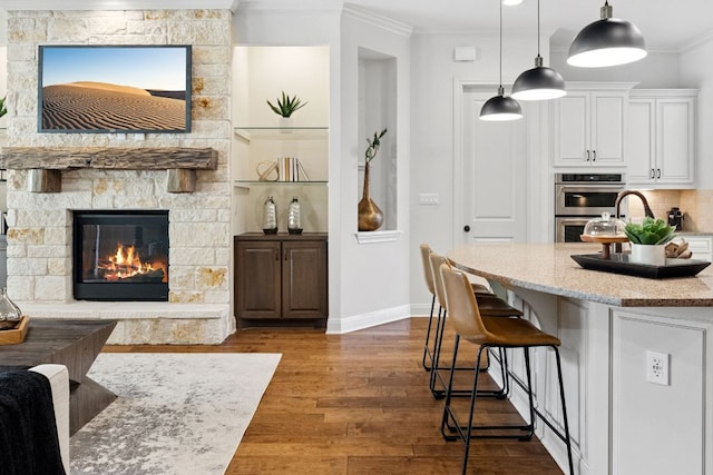 377 Bristlecone Dr, Driftwood, TX 78619 - kitchen featuring double oven, white cabinetry, ornamental molding, a kitchen breakfast bar, and dark wood-style flooring