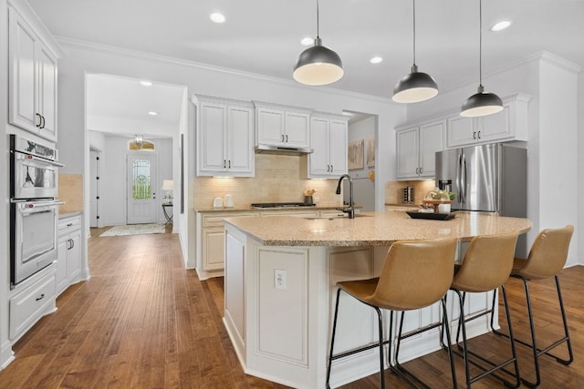 377 Bristlecone Dr, Driftwood, TX 78619 - kitchen featuring appliances with stainless steel finishes, under cabinet range hood, backsplash, ornamental molding, and an island with sink