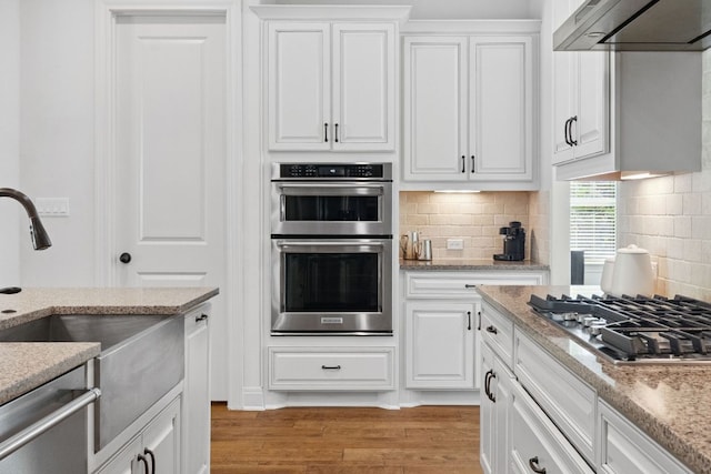 377 Bristlecone Dr, Driftwood, TX 78619 - kitchen with extractor fan, stainless steel appliances, light wood-style flooring, white cabinets, and backsplash