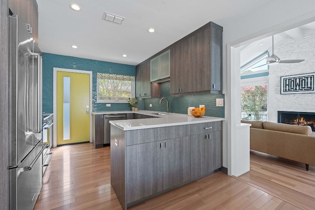 4405 Greystone Dr, Austin, TX 78731 - kitchen with appliances with stainless steel finishes, a peninsula, light wood finished floors, light countertops, and a stone fireplace