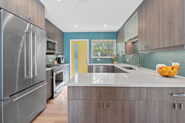 4405 Greystone Dr, Austin, TX 78731 - kitchen featuring premium appliances, light countertops, a peninsula, backsplash, and light wood-style flooring