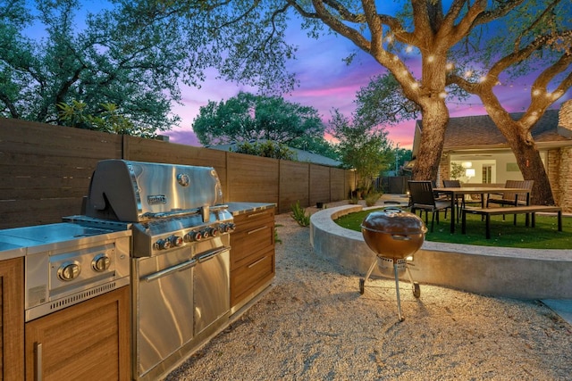 4405 Greystone Dr, Austin, TX 78731 - patio terrace at dusk featuring a fenced backyard, an outdoor kitchen, outdoor dining space, and a patio
