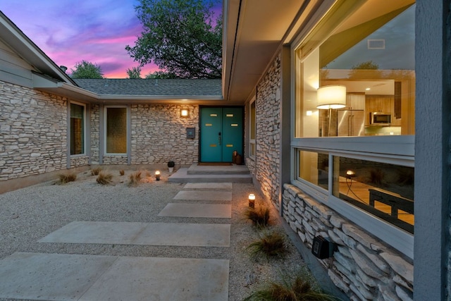 4405 Greystone Dr, Austin, TX 78731 - exterior entry at dusk featuring stone siding and a shingled roof