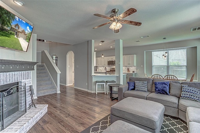 2712 Kickapoo Cavern Dr, Pflugerville, TX 78660 - living area featuring arched walkways, dark wood-style floors, ceiling fan, a fireplace, and stairs