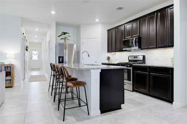 114 Creek Hollow Dr, Hutto, TX 78634 - kitchen featuring stainless steel appliances, tasteful backsplash, light stone counters, an island with sink, and a breakfast bar area