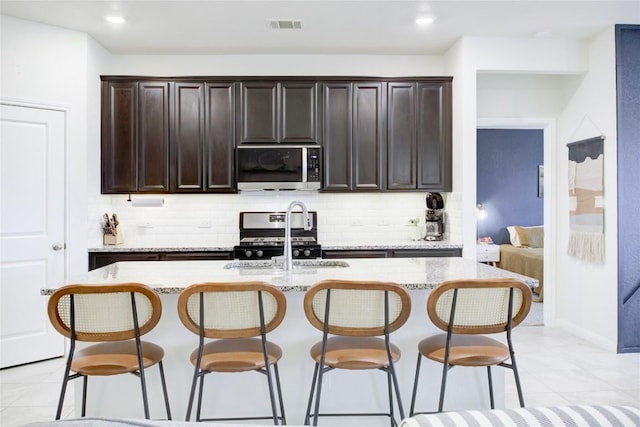 114 Creek Hollow Dr, Hutto, TX 78634 - kitchen with appliances with stainless steel finishes, decorative backsplash, a breakfast bar area, an island with sink, and light tile patterned floors