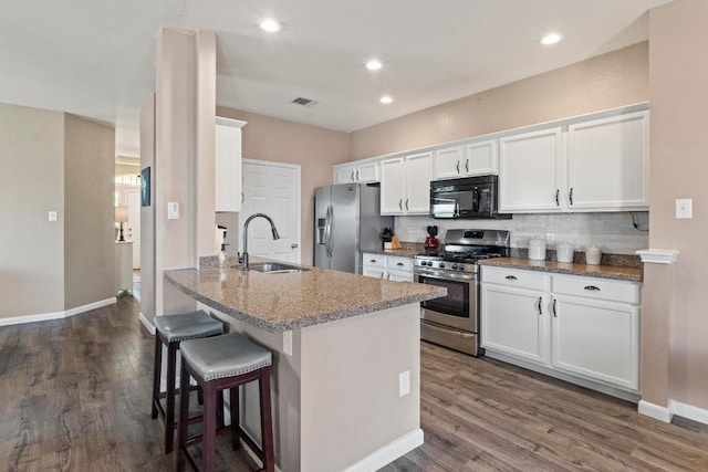 1111 Whitley Dr, Leander, TX 78641 - kitchen with appliances with stainless steel finishes, white cabinets, dark wood finished floors, a breakfast bar area, and recessed lighting