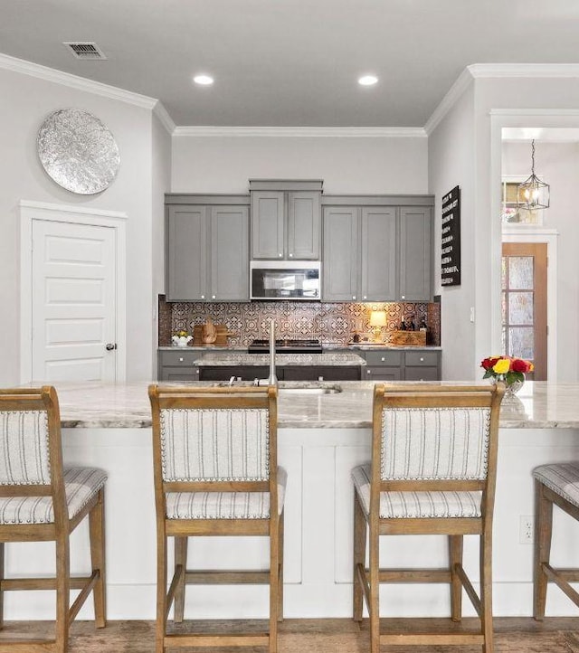 4 Country Ct, Wimberley, TX 78676 - kitchen featuring stainless steel microwave, gray cabinetry, decorative backsplash, light stone countertops, and crown molding