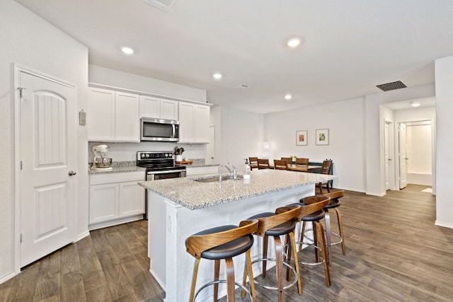 1004 Norway, Seguin, TX 78155 - kitchen featuring appliances with stainless steel finishes, a breakfast bar area, dark wood finished floors, white cabinets, and recessed lighting