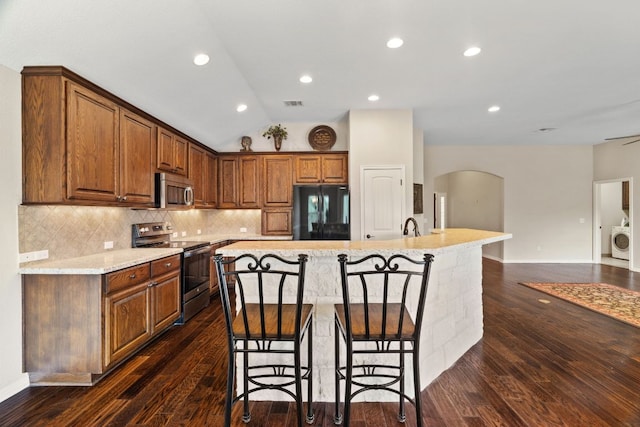 1403 Adam Ave, Burnet, TX 78611 - kitchen with stainless steel appliances, washer / dryer, arched walkways, a center island with sink, and a kitchen bar