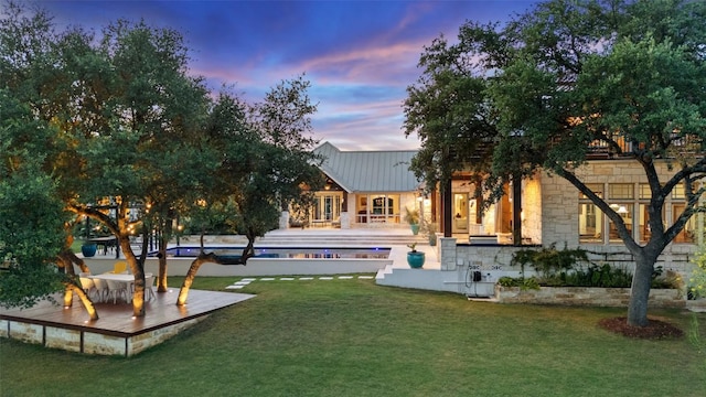 601 Crystal Creek Dr, Austin, TX 78746 - back of house at dusk featuring stone siding, a lawn, and a wooden deck