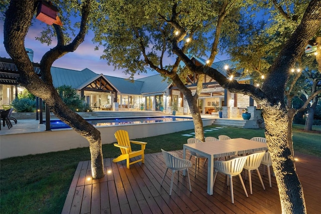 601 Crystal Creek Dr, Austin, TX 78746 - pool at dusk with outdoor dining space, an outdoor pool, a wooden deck, and a lawn