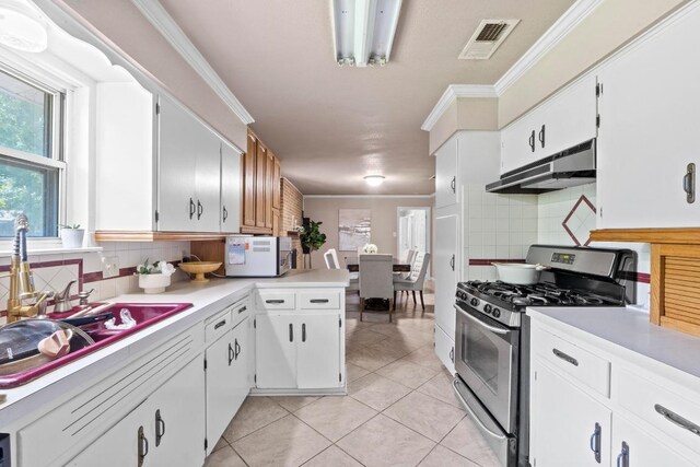11907 Oak Trl, Austin, TX 78753 - kitchen featuring stainless steel gas stove, under cabinet range hood, light tile patterned floors, decorative backsplash, and ornamental molding