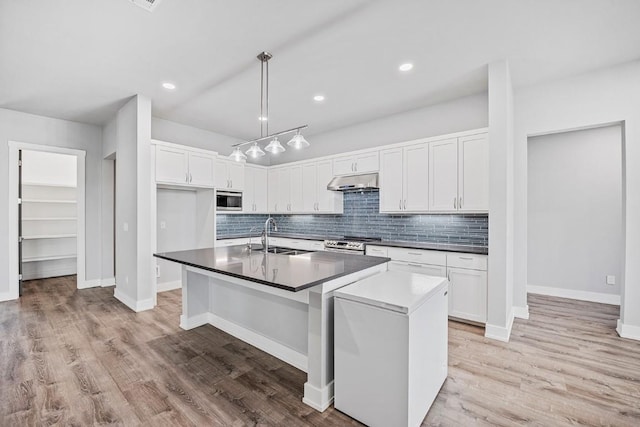 21603 Thomas Cv, Lago Vista, TX 78645 - kitchen featuring stainless steel appliances, dark countertops, backsplash, white cabinetry, and a center island with sink