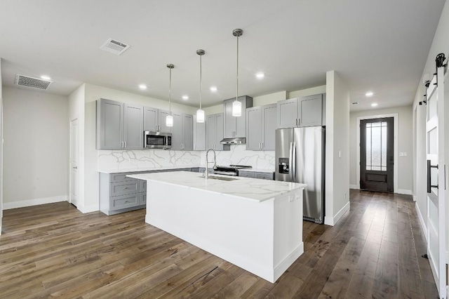 182 Alonzo Dr, Del Valle, TX 78617 - kitchen featuring appliances with stainless steel finishes, a barn door, gray cabinets, decorative backsplash, and recessed lighting