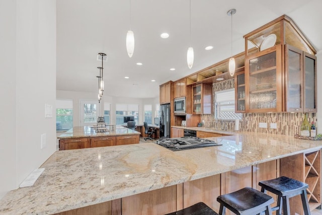 815 Clarence Bohls Ln, Pflugerville, TX 78660 - kitchen with stainless steel microwave, freestanding refrigerator, gas cooktop, brown cabinetry, and light stone countertops