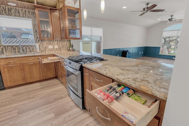 815 Clarence Bohls Ln, Pflugerville, TX 78660 - kitchen with stainless steel gas stove, brown cabinetry, lofted ceiling, wainscoting, and ceiling fan