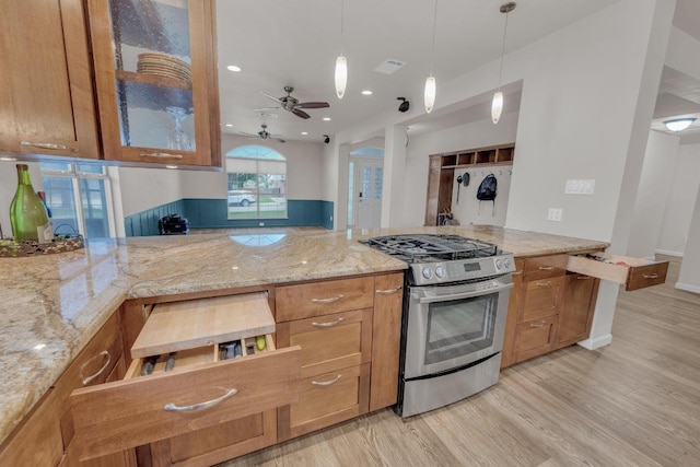 815 Clarence Bohls Ln, Pflugerville, TX 78660 - kitchen with gas range, brown cabinetry, light wood-type flooring, ceiling fan, and light stone countertops