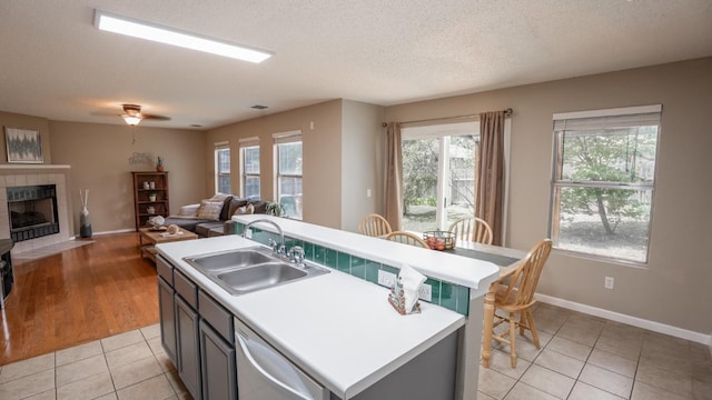 8086 Thaxton Rd, Austin, TX 78747 - kitchen featuring white dishwasher, a tile fireplace, light tile patterned floors, an island with sink, and light countertops