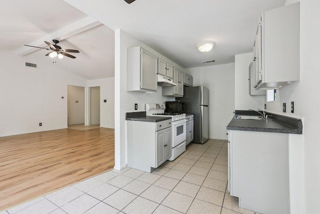 1613 J J Seabrook Dr, Austin, TX 78721 - kitchen featuring white gas range, under cabinet range hood, freestanding refrigerator, a ceiling fan, and dark countertops
