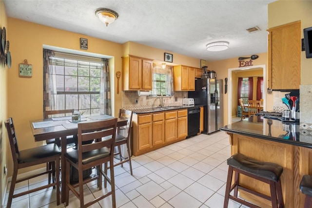 5804 Sheffield Terrace Ln, Bryan, TX 77802 - kitchen featuring black dishwasher, refrigerator with ice dispenser, backsplash, dark countertops, and a textured ceiling