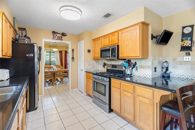 5804 Sheffield Terrace Ln, Bryan, TX 77802 - kitchen with appliances with stainless steel finishes, backsplash, light tile patterned flooring, a breakfast bar area, and dark stone counters