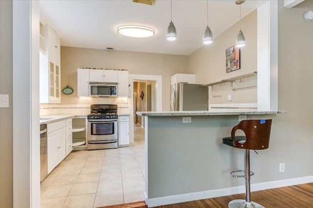 4415 Ave D Ave, Austin, TX 78751 - kitchen featuring appliances with stainless steel finishes, white cabinetry, a kitchen bar, a peninsula, and decorative light fixtures