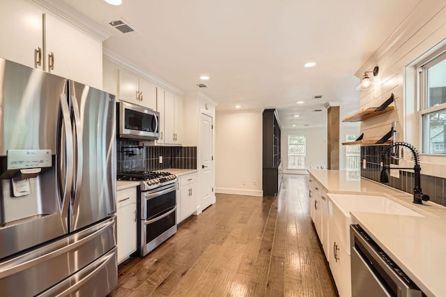 1511 Wilson Heights Dr, Austin, TX 78746 - kitchen with stainless steel appliances, light countertops, white cabinets, backsplash, and wood finished floors