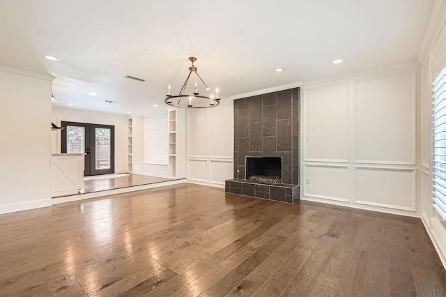 1511 Wilson Heights Dr, Austin, TX 78746 - unfurnished living room featuring hardwood / wood-style flooring, built in features, a chandelier, ornamental molding, and a tile fireplace