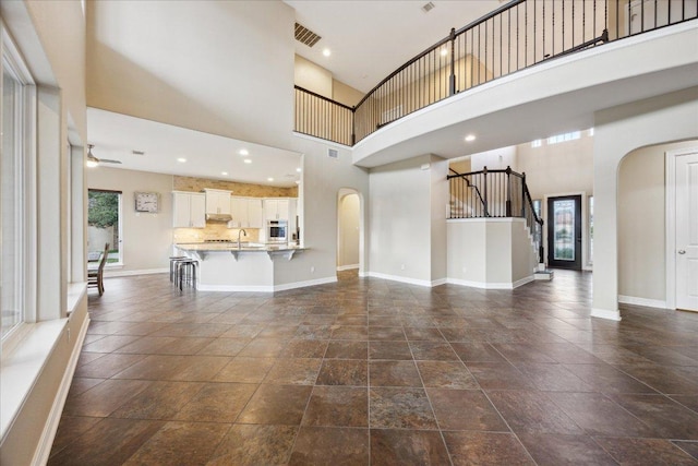 3207 Crystal Falls Pkwy, Leander, TX 78641 - unfurnished living room featuring arched walkways, a towering ceiling, stone tile flooring, ceiling fan, and stairway