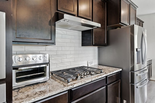 8100 Copper Prairie Bnd, Lago Vista, TX 78645 - kitchen featuring appliances with stainless steel finishes, under cabinet range hood, dark brown cabinets, tasteful backsplash, and light stone countertops