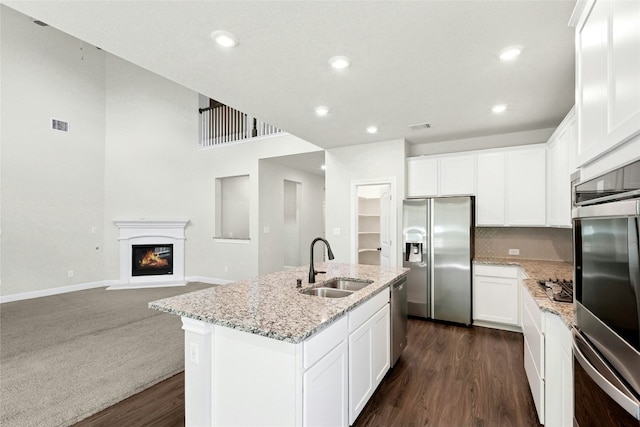 2309 Lone Spur Cv, Round Rock, TX 78665 - kitchen with appliances with stainless steel finishes, light stone countertops, a center island with sink, a glass covered fireplace, and dark wood-style floors