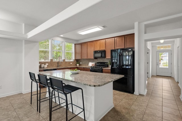 1267 Sanders, Kyle, TX 78640 - kitchen with black appliances, a kitchen island, backsplash, a breakfast bar, and light tile patterned flooring