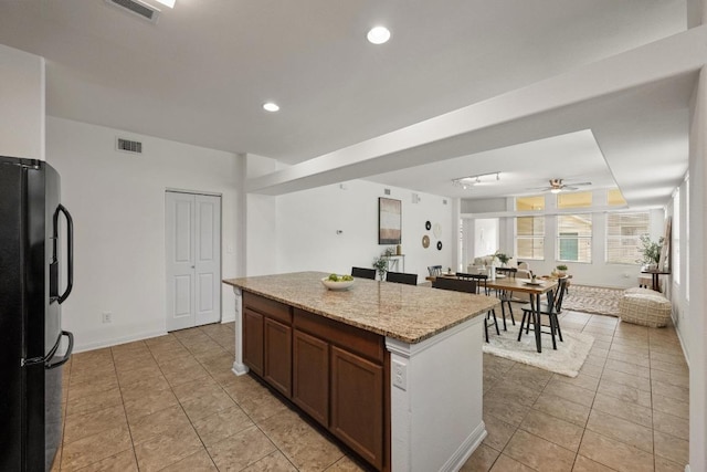 1267 Sanders, Kyle, TX 78640 - kitchen featuring freestanding refrigerator, light tile patterned floors, a kitchen island, a ceiling fan, and light stone countertops