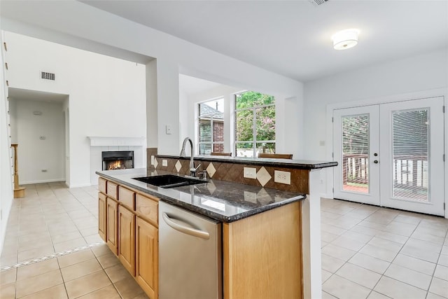 12608 Chittim Cir, Austin, TX 78732 - kitchen featuring dishwasher, light tile patterned floors, a tiled fireplace, a center island with sink, and dark stone countertops