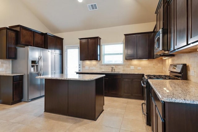 632 Schefer St, Leander, TX 78641 - kitchen with appliances with stainless steel finishes, dark brown cabinetry, vaulted ceiling, light stone counters, and backsplash