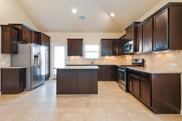 632 Schefer St, Leander, TX 78641 - kitchen with appliances with stainless steel finishes, lofted ceiling, dark brown cabinets, a kitchen island, and light stone counters