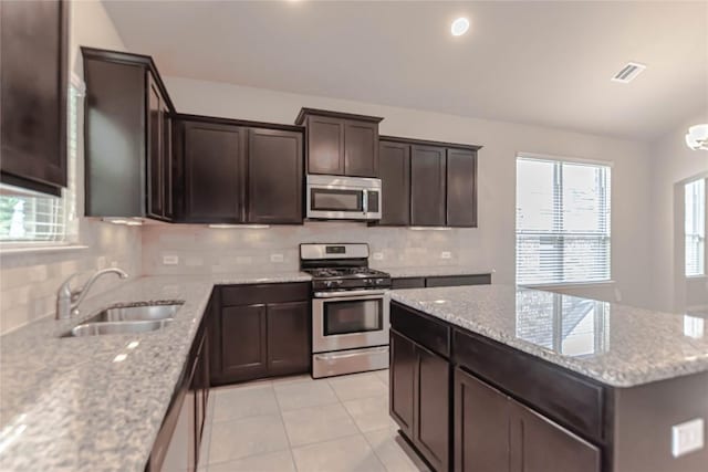 632 Schefer St, Leander, TX 78641 - kitchen with stainless steel appliances, tasteful backsplash, light tile patterned floors, dark brown cabinets, and light stone countertops
