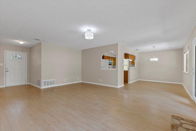 901 Pack Saddle Pass, Round Rock, TX 78681 - unfurnished living room with light wood-style floors, a textured ceiling, and a chandelier