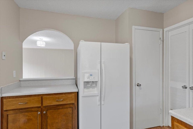 901 Pack Saddle Pass, Round Rock, TX 78681 - kitchen with white refrigerator with ice dispenser, brown cabinetry, arched walkways, light countertops, and a textured ceiling
