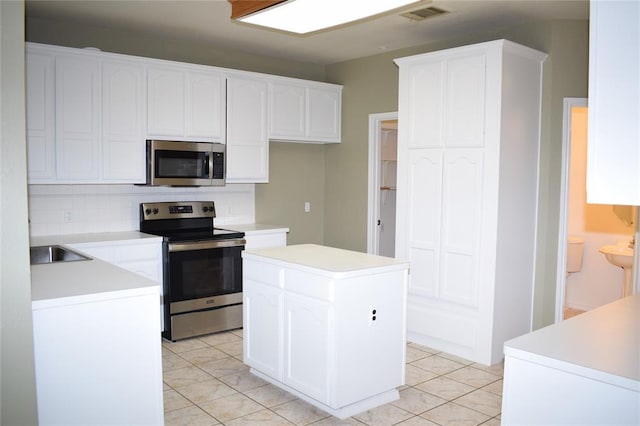 30007 Oakland Hills Dr, Georgetown, TX 78628 - kitchen with appliances with stainless steel finishes, tasteful backsplash, white cabinets, a kitchen island, and light tile patterned flooring