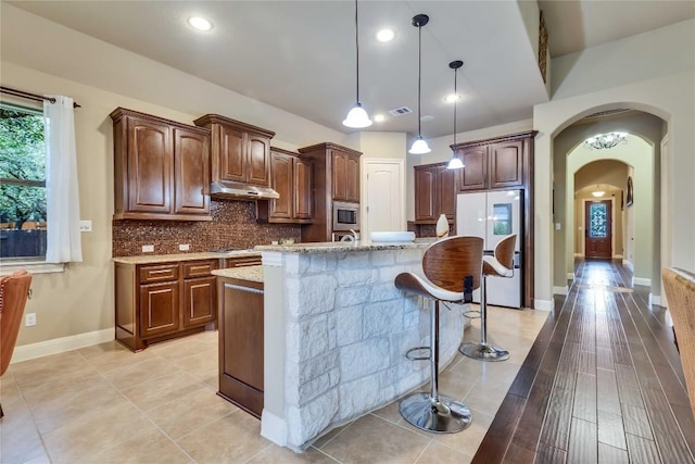 4108 Charbray Ct, Cedar Park, TX 78613 - kitchen featuring stainless steel appliances, under cabinet range hood, arched walkways, tasteful backsplash, and light stone countertops
