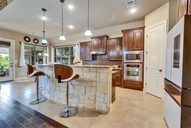 4108 Charbray Ct, Cedar Park, TX 78613 - kitchen featuring appliances with stainless steel finishes, under cabinet range hood, a kitchen bar, backsplash, and light stone counters