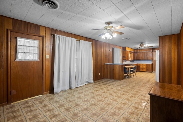 1213 Norbert St, Marlin, TX 76661 - kitchen with brown cabinets, a peninsula, wood walls, a ceiling fan, and a kitchen breakfast bar
