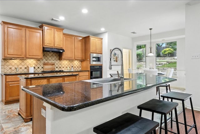 5704 Keli Ct, Austin, TX 78735 - kitchen featuring stainless steel microwave, black oven, an island with sink, tasteful backsplash, and a breakfast bar area