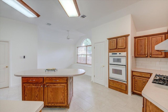 6604 Donner Cv, Austin, TX 78749 - kitchen featuring double oven, brown cabinets, light countertops, a center island, and vaulted ceiling