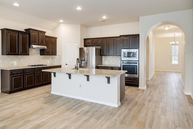 285 Chisholm Trl, Bastrop, TX 78602 - kitchen featuring stainless steel appliances, arched walkways, under cabinet range hood, a kitchen breakfast bar, and decorative backsplash
