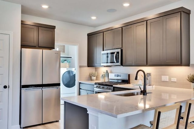 2235 Oscar Eli Way, Round Rock, TX 78665 - kitchen featuring appliances with stainless steel finishes, a peninsula, light stone counters, backsplash, and a kitchen breakfast bar