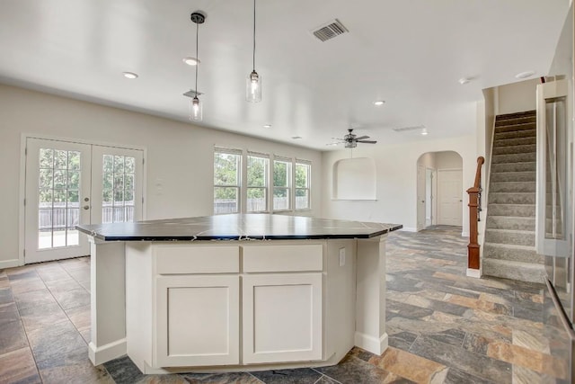309 Camperdown Elm Dr, Austin, TX 78748 - kitchen with arched walkways, stone tile floors, dark countertops, white cabinets, and a center island